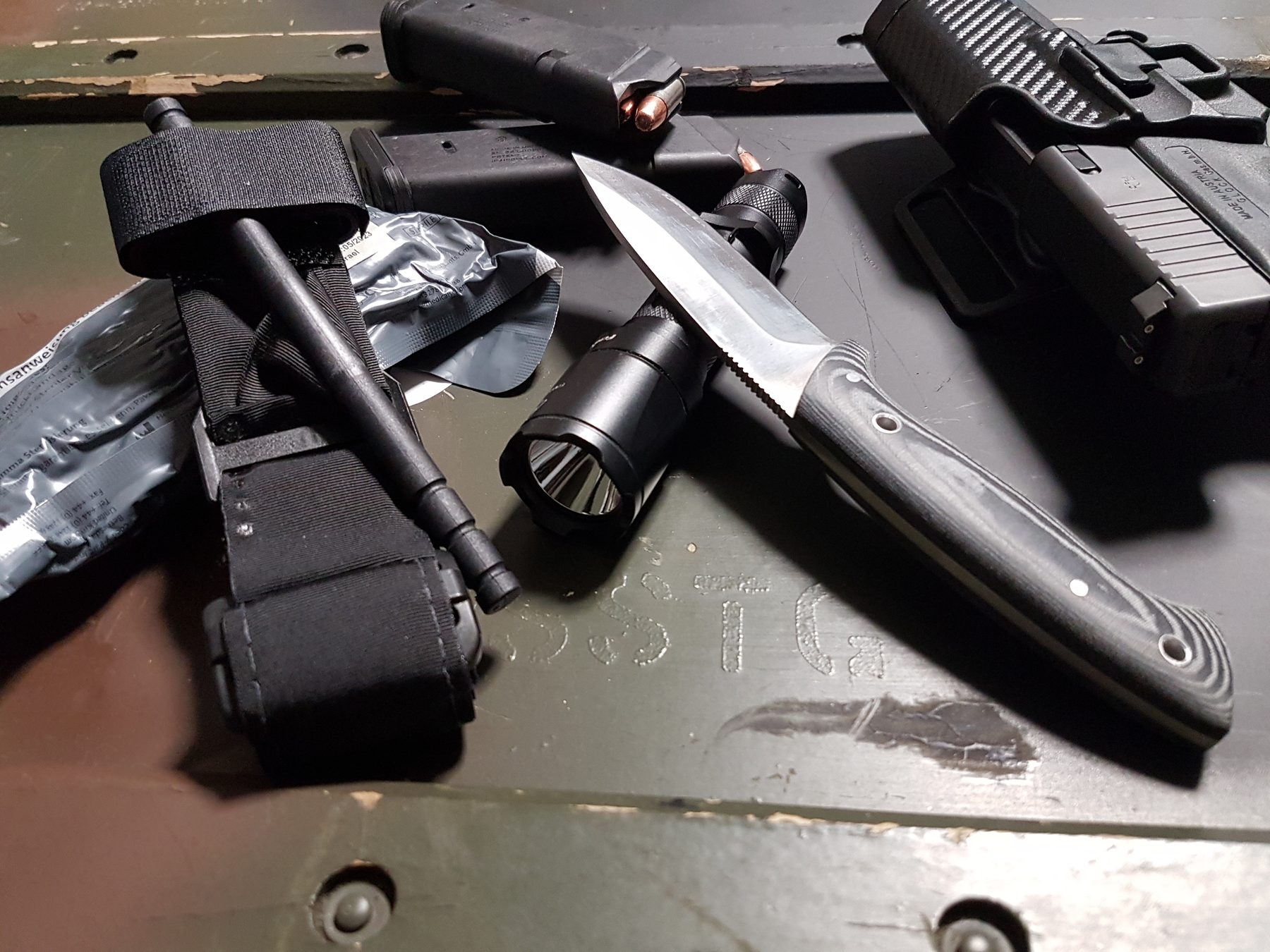 Verbandmaterial mit Tourniquet, Taschenlampe und Kurzwaffe im Holster auf einer Kiste.