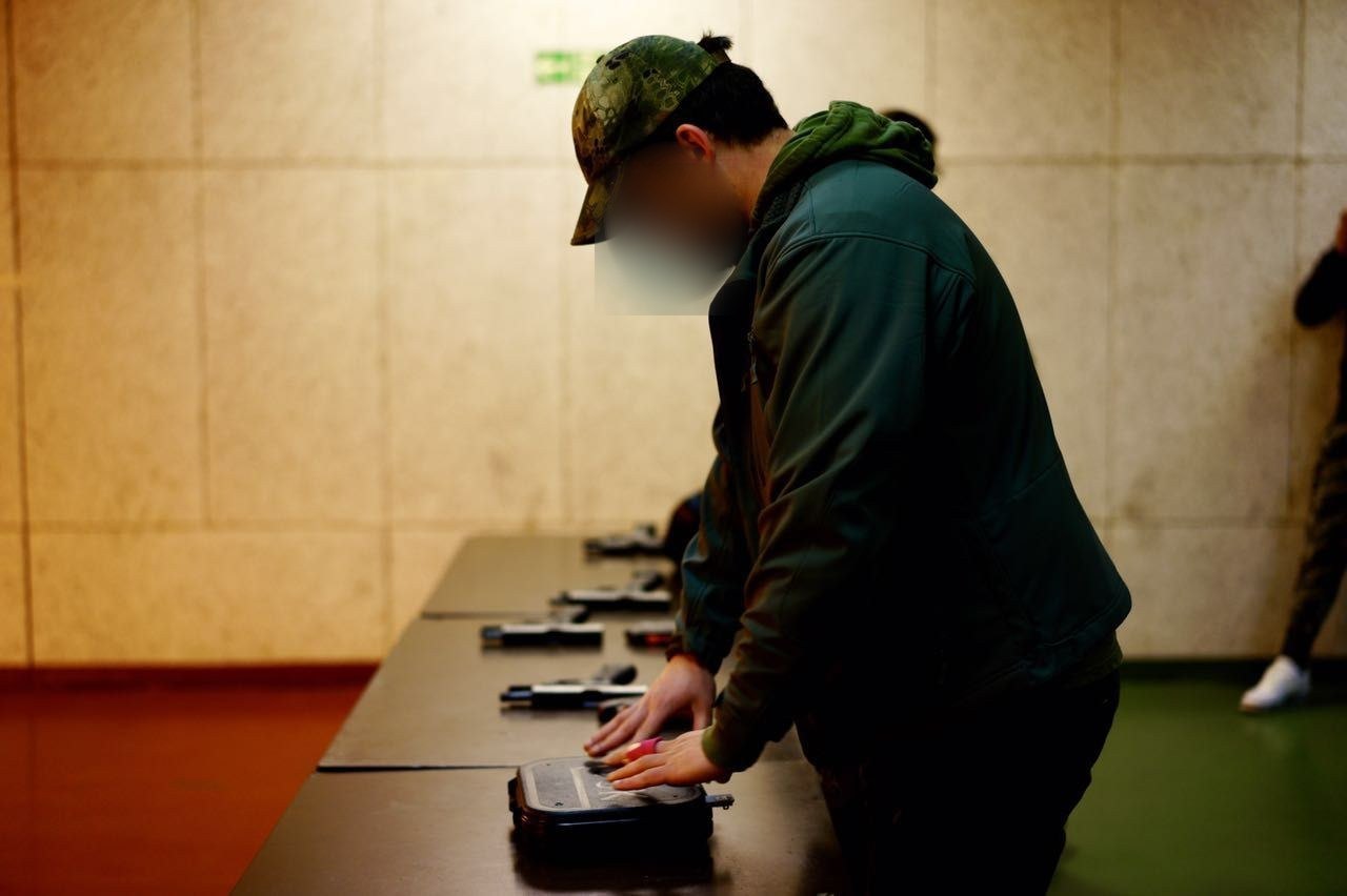 Teilnehmer legt die Kurzwaffe im Koffer ab, Gesicht unkenntlich gemacht.
